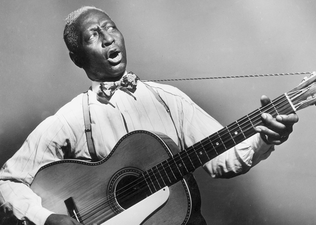 Promotional portrait of Leadbelly Ledbetter singing with guitar.