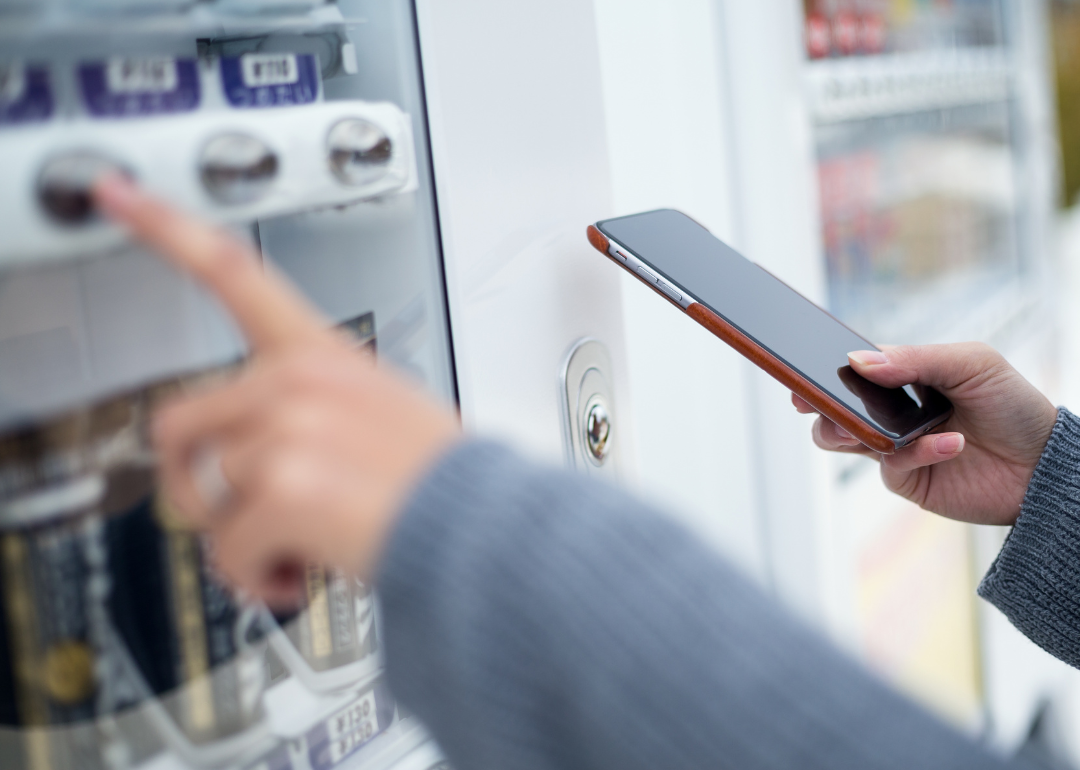 Person using cellphone at vending machine.