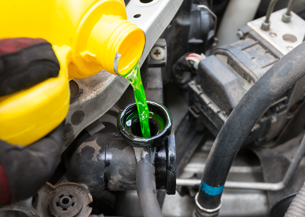A gloved hand pouring a yellow bottle of coolant fluid into an engine.
