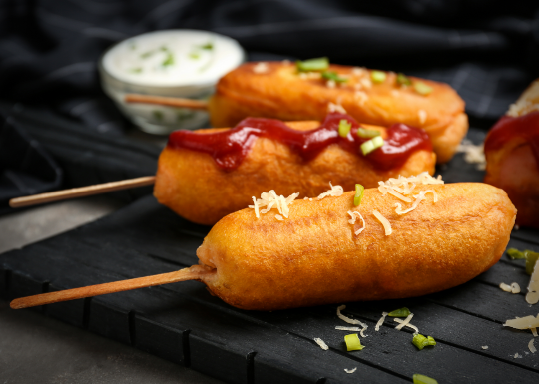 Corn dogs with ketchup on board, sprinkled with parmesan and green onions.