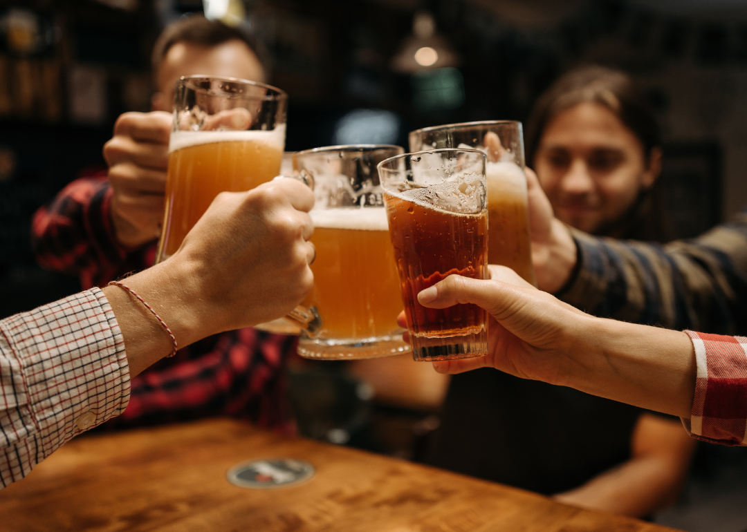People raise beer glasses together at bar.