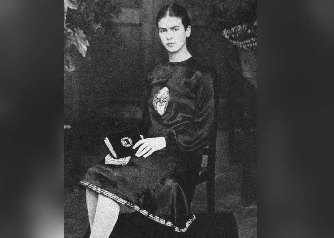 Frida Kahlo as a student, sitting in a chair and holding a book.