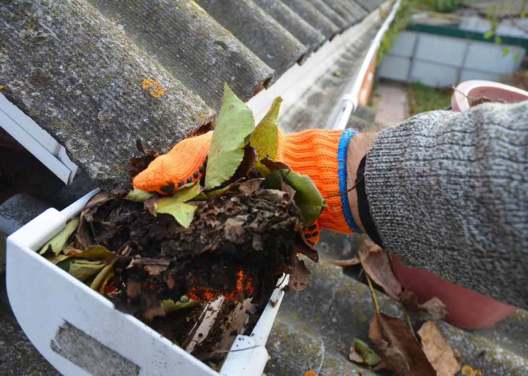 A cropped view of person cleaning a clogged roof gutter.