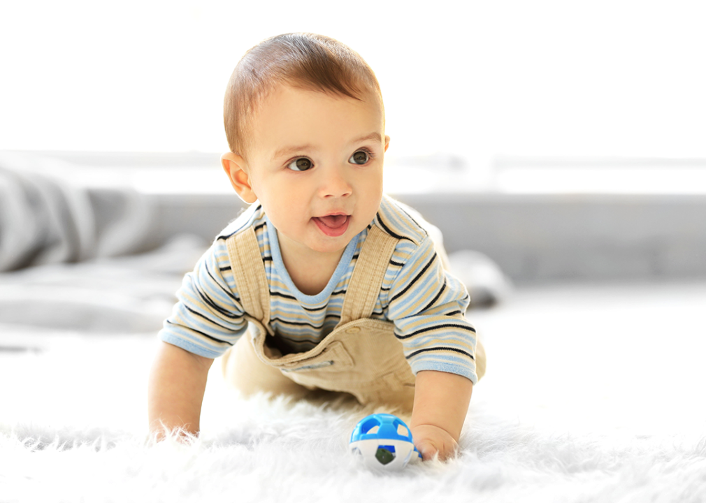 Baby crawling on carpet holding toy.