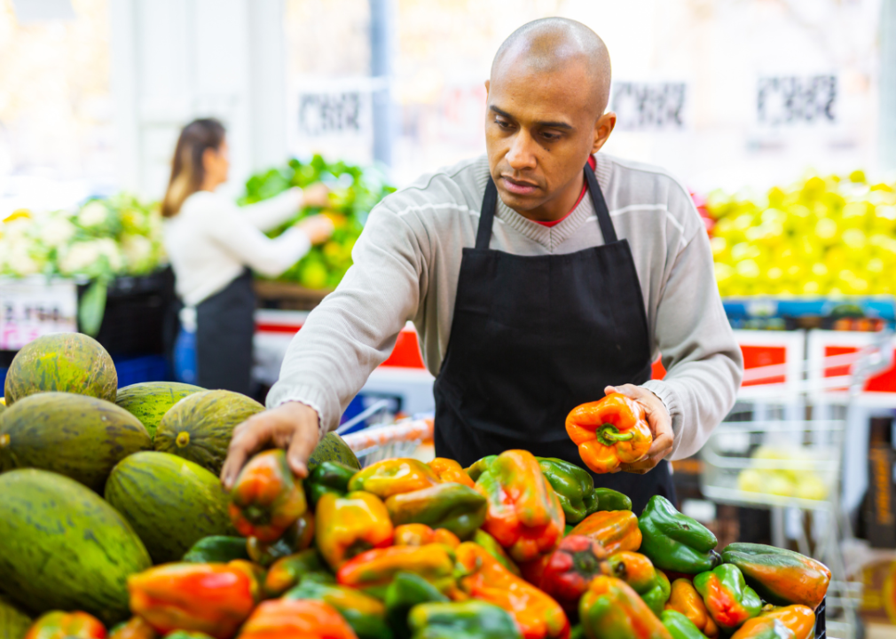 Supermarket employee in apron checks produce in vegetable section