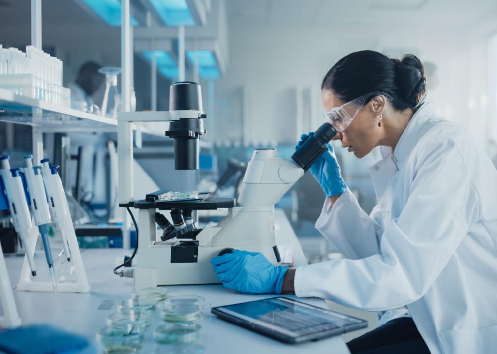 Scientist in laboratory with laptop and microscope.