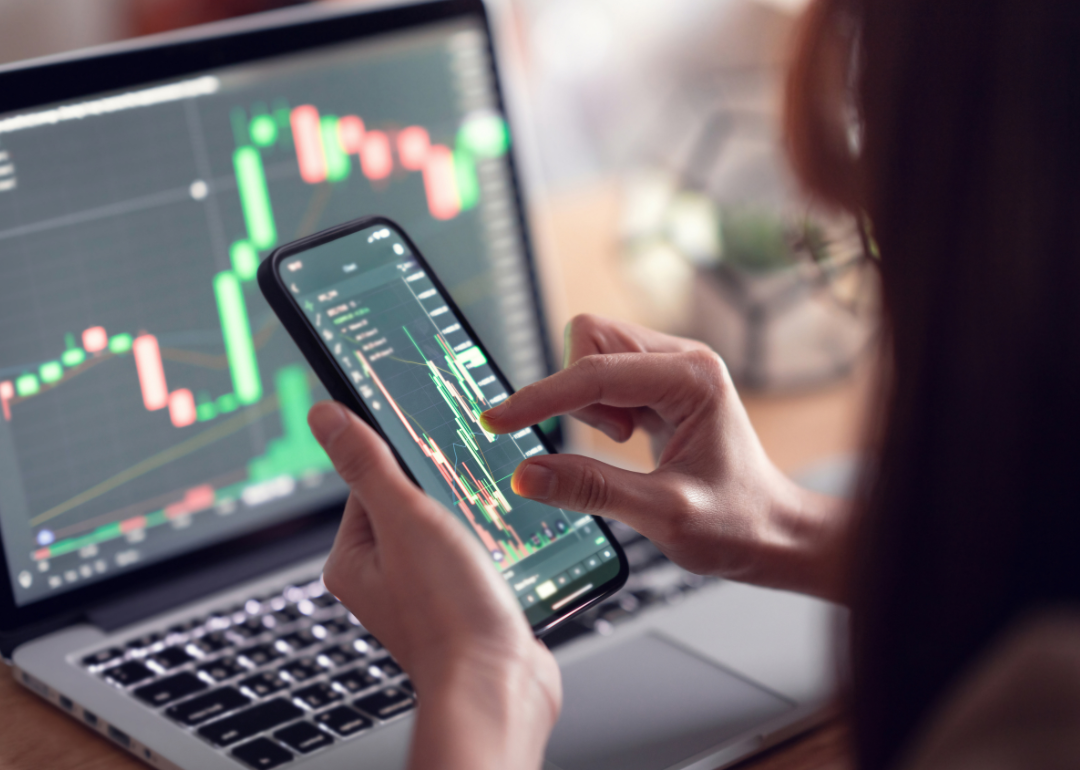 Person using phone looking at trading chart on laptop