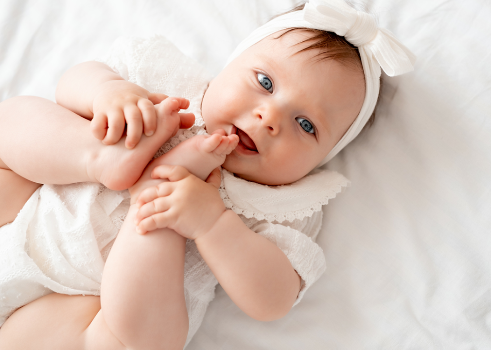 Baby laying on back holding feet.