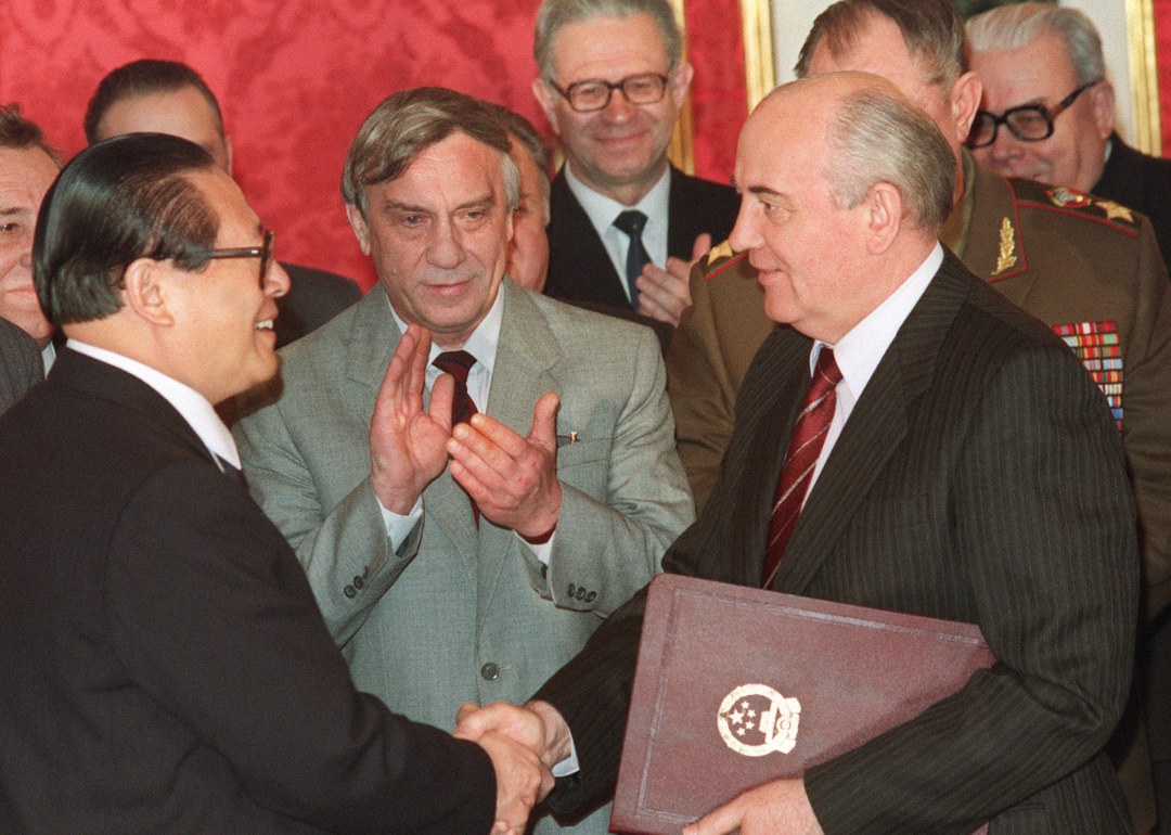 Mikhail Gorbachev holding documents shakes hands with Jiang Zemin as others applaud