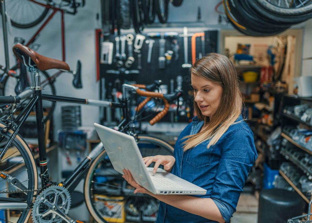 Small business owner holding laptop in repair shop.