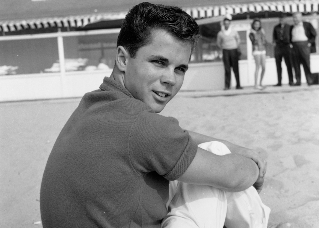 Tony Dow looks over his shoulder while sitting on a beach.