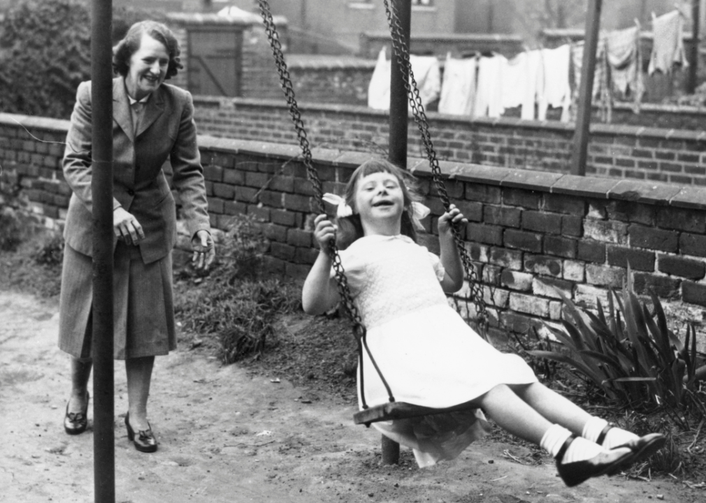 Mother pushes daughter on swing.
