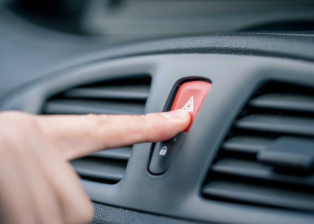 Person pushing hazard light button in car.