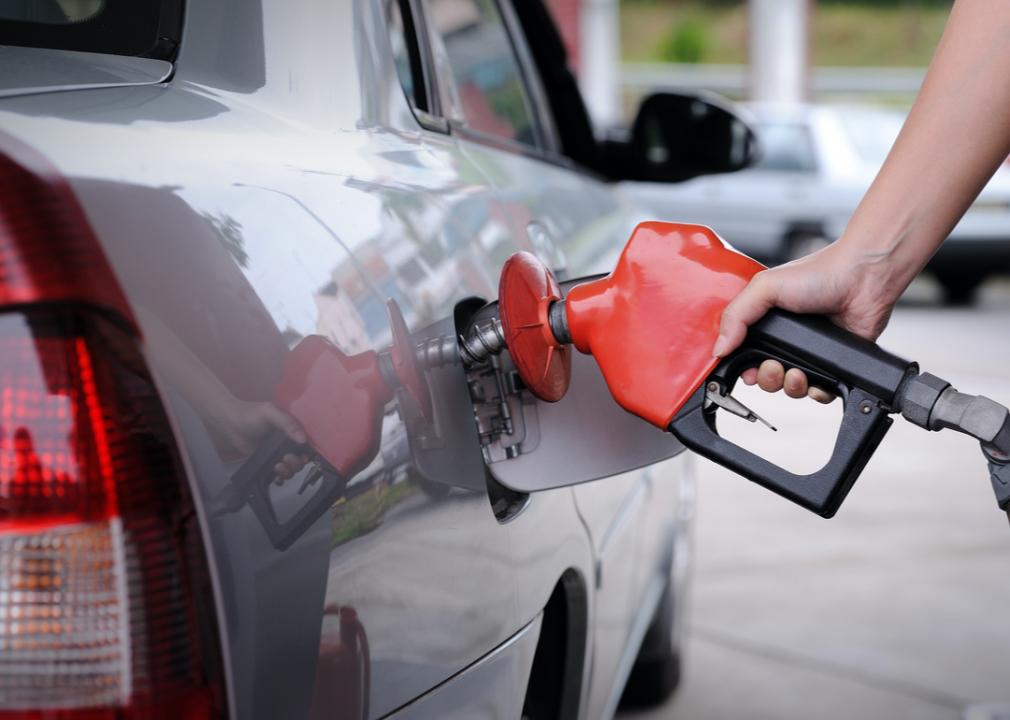 Photo shows a close-up of a hand pumping gas into a vehicle at a gas station