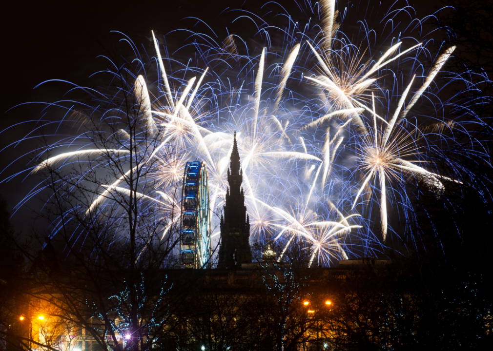 Fireworks emerge behind the Christmas market ferris wheel and the Sir Walter Scott monument. 