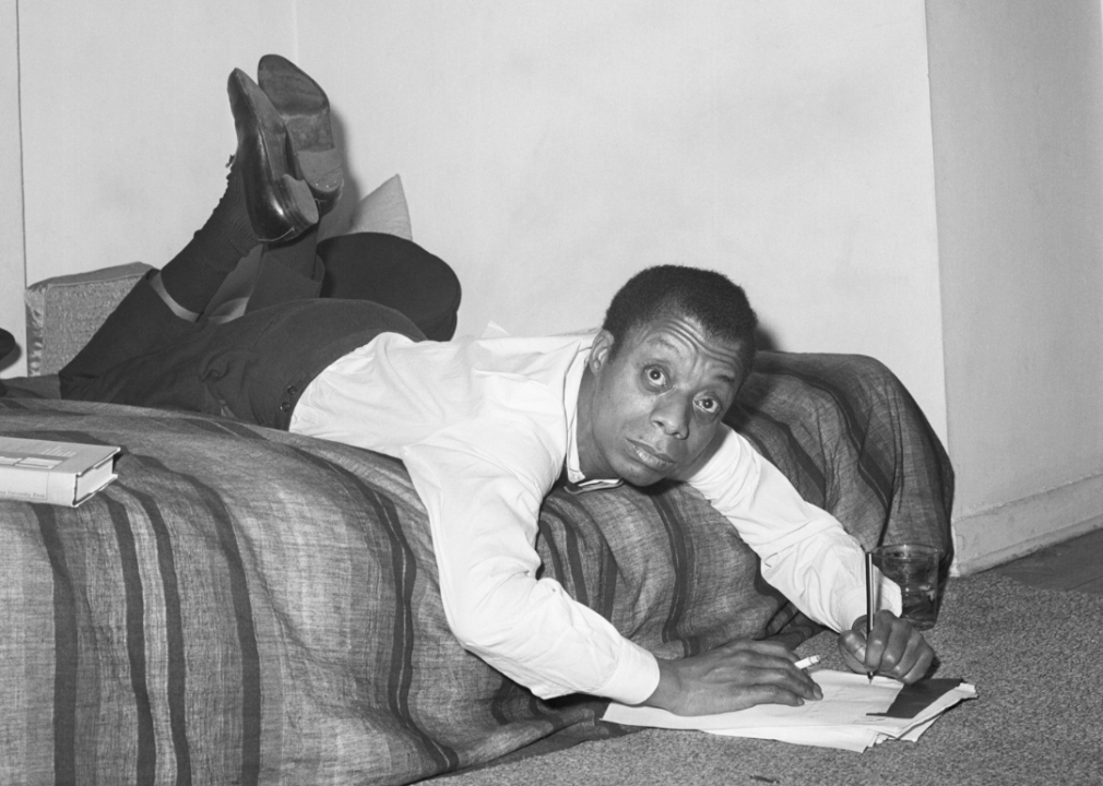 James Baldwin leaning over a bed writing notes.