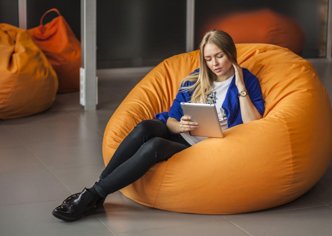Woman in orange beanbag chair reading tablet.