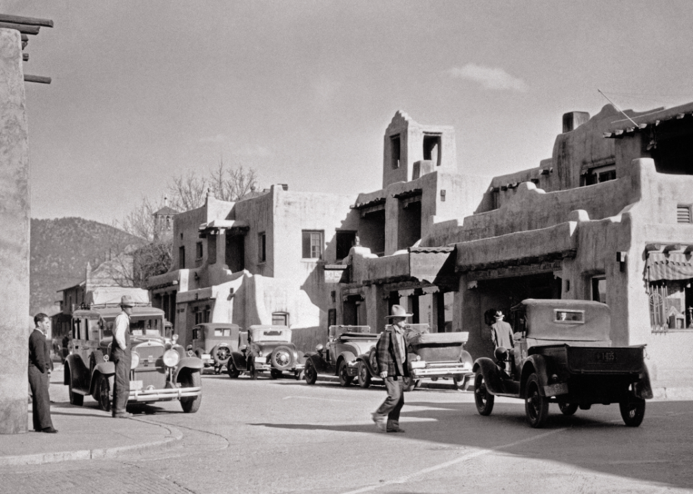 Pedestrians, automobiles, and trucks in street in front of La Fonda Hotel.