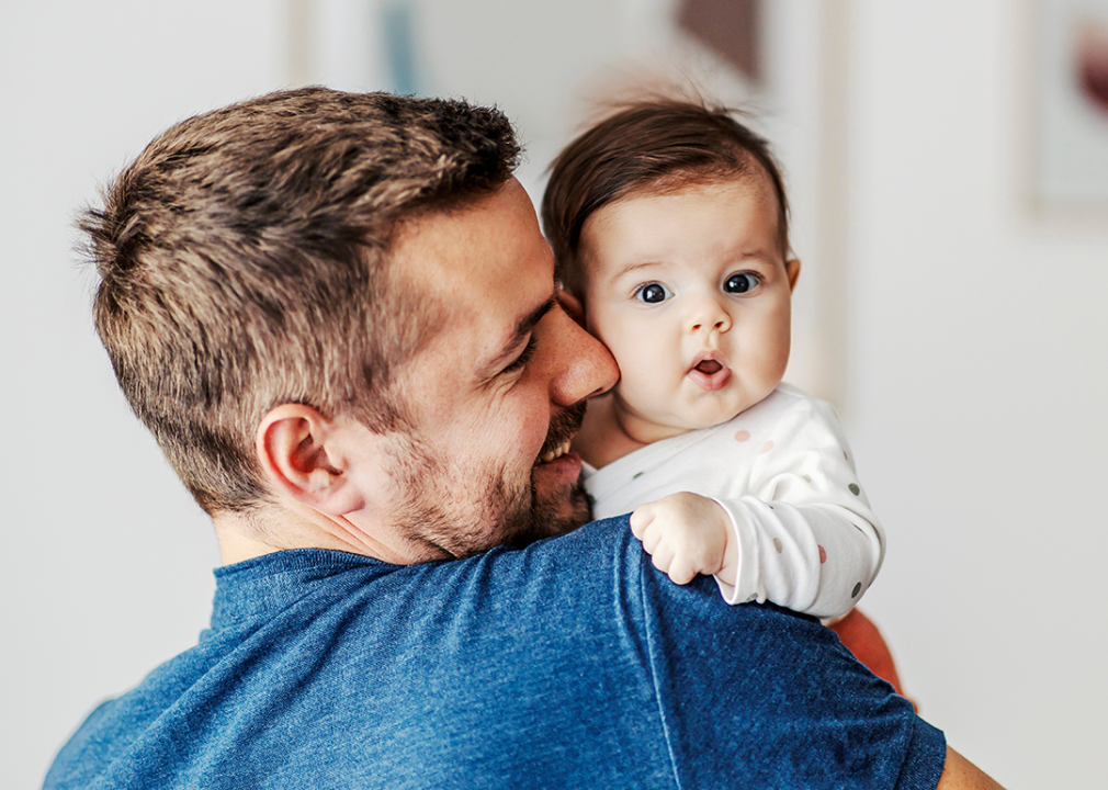 Baby in father’s arms looking at camera with surprised expression.