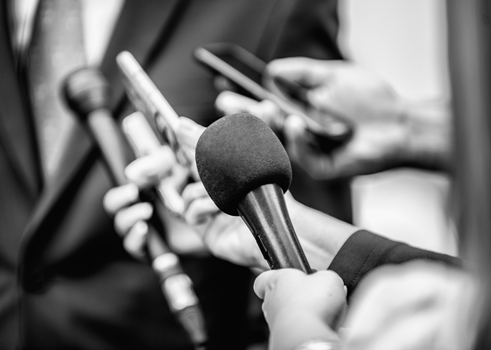 Journalists with microphones interviewing person wearing suit.