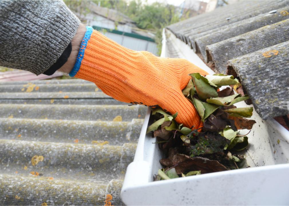 Photo shows a close-up of a gloved hand clearing debris from a house storm gutter