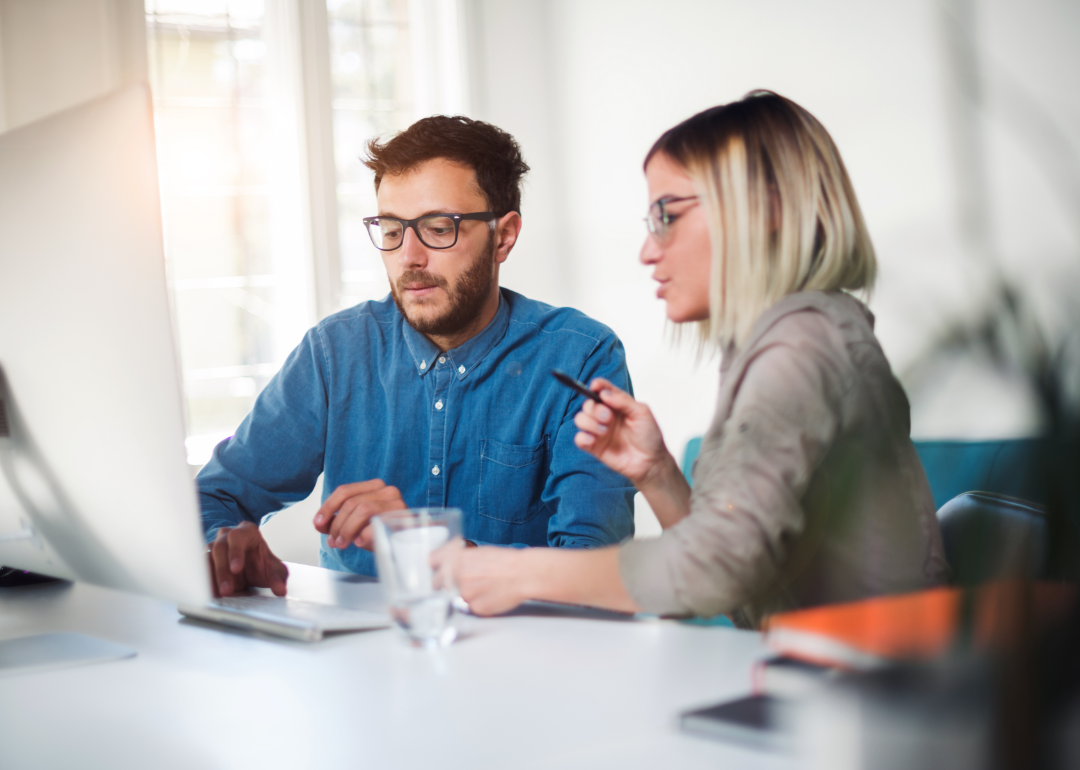 Two professionals working at desktop computer having discussion.