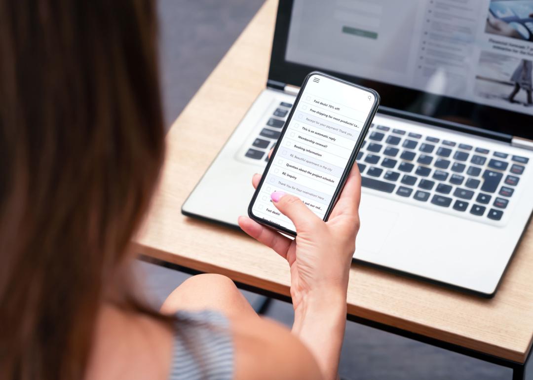 Person looking at email on phone with laptop open.