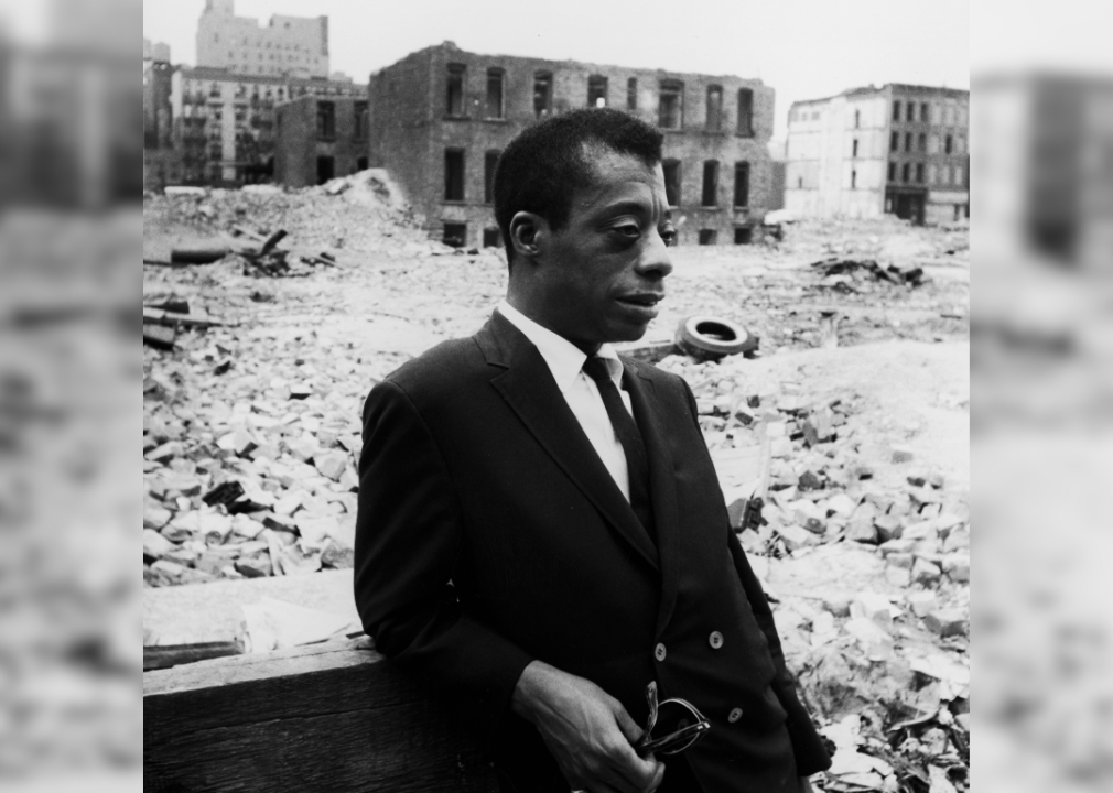 James Baldwin standing in the middle of demolished buildings and rubble.