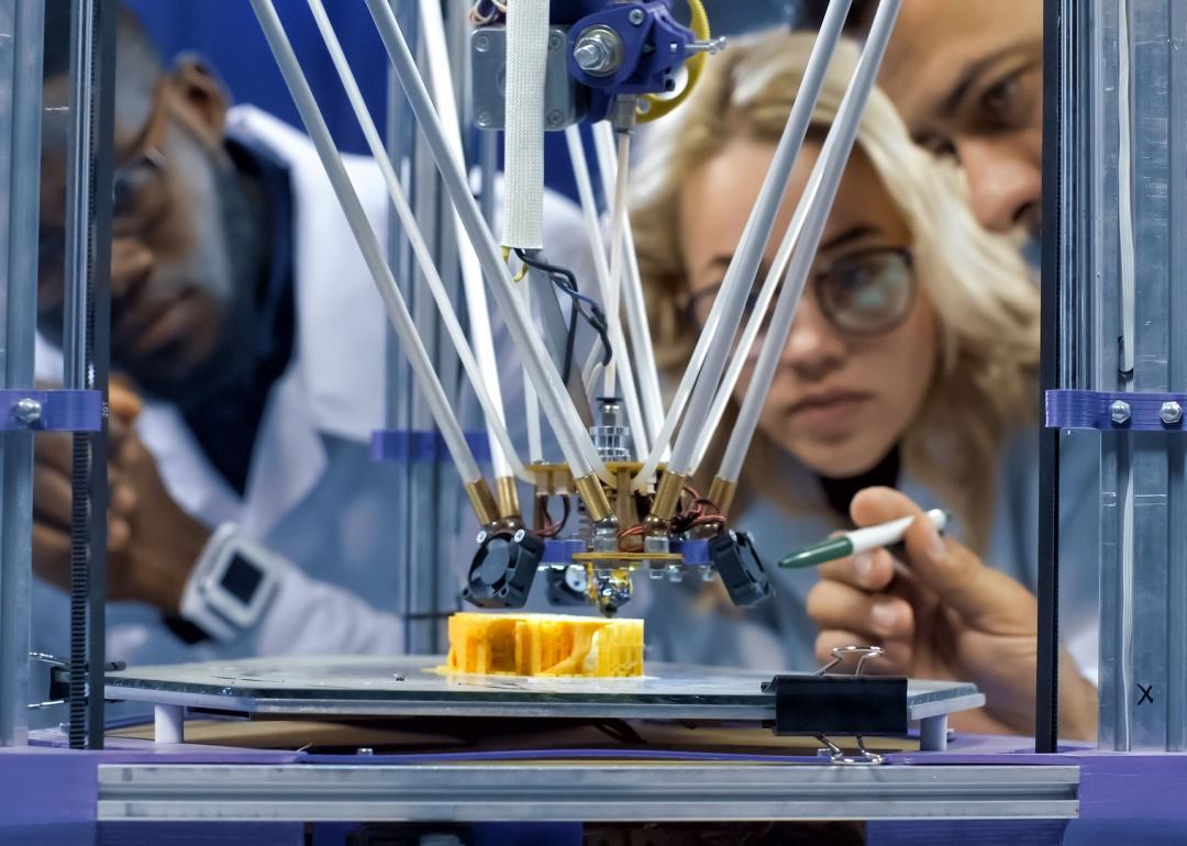 People gathered around 3D printer watching model production.