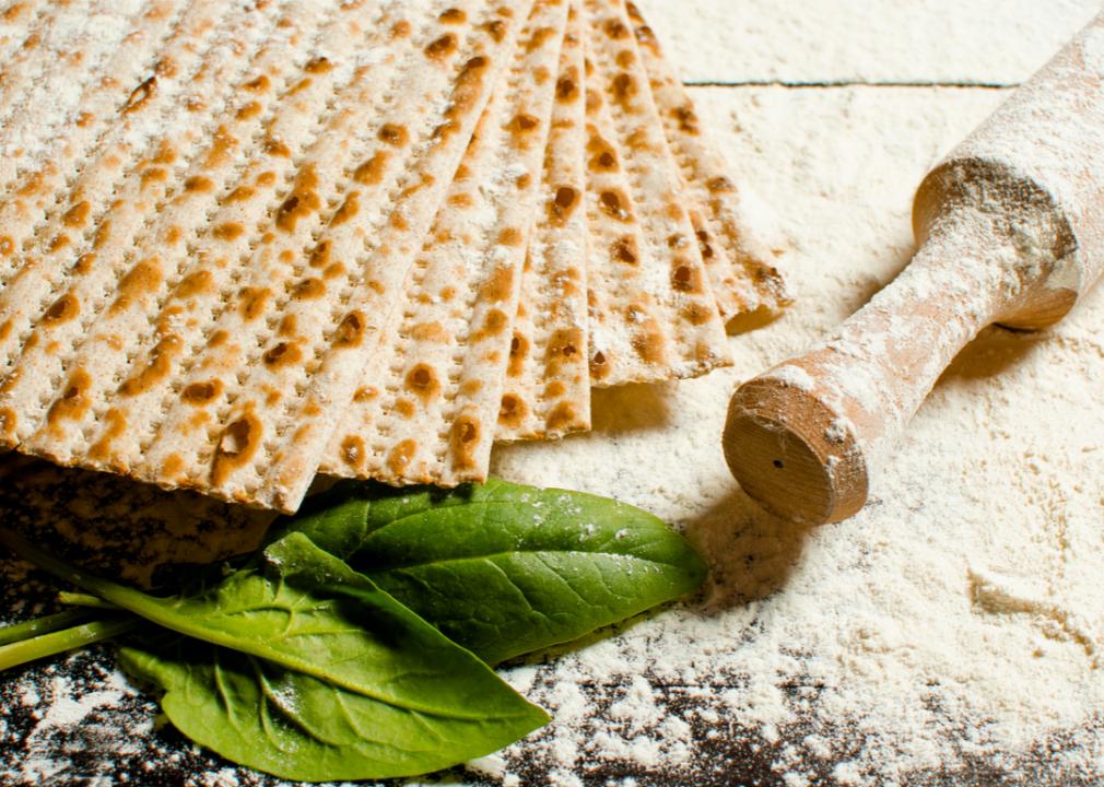 Flour-dusted matzo next to a rolling pin on a floured surface. 