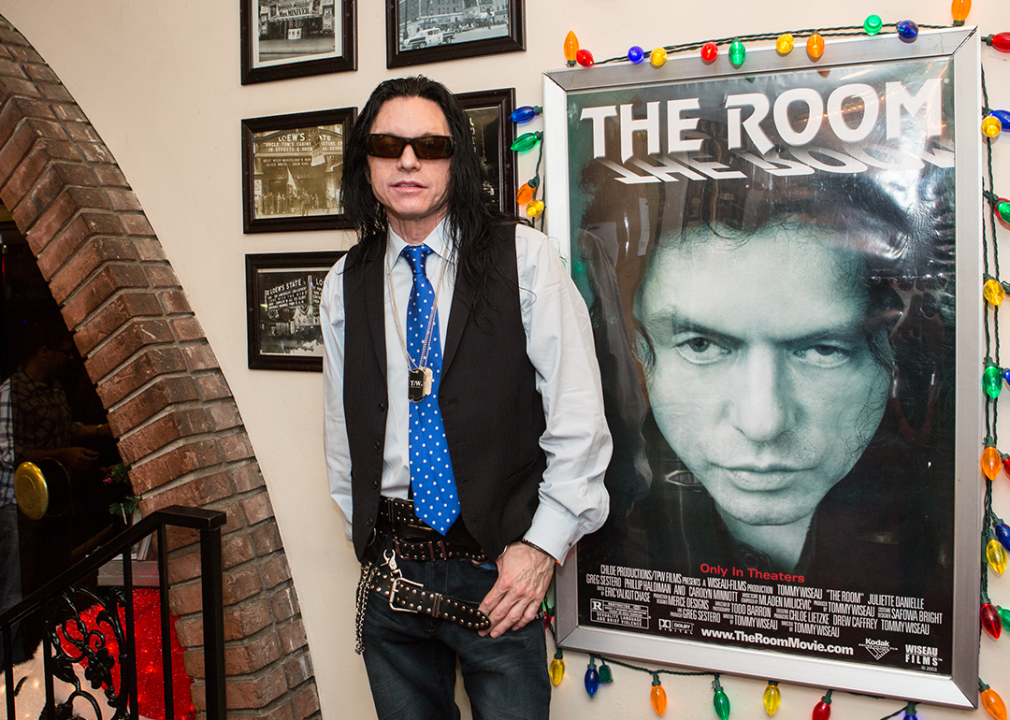 Tommy Wiseau poses next to a poster for 