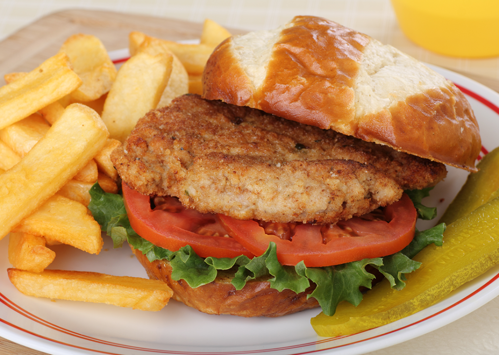 Pork tenderloin, lettuce and tomato sandwich on a bun with french fries.