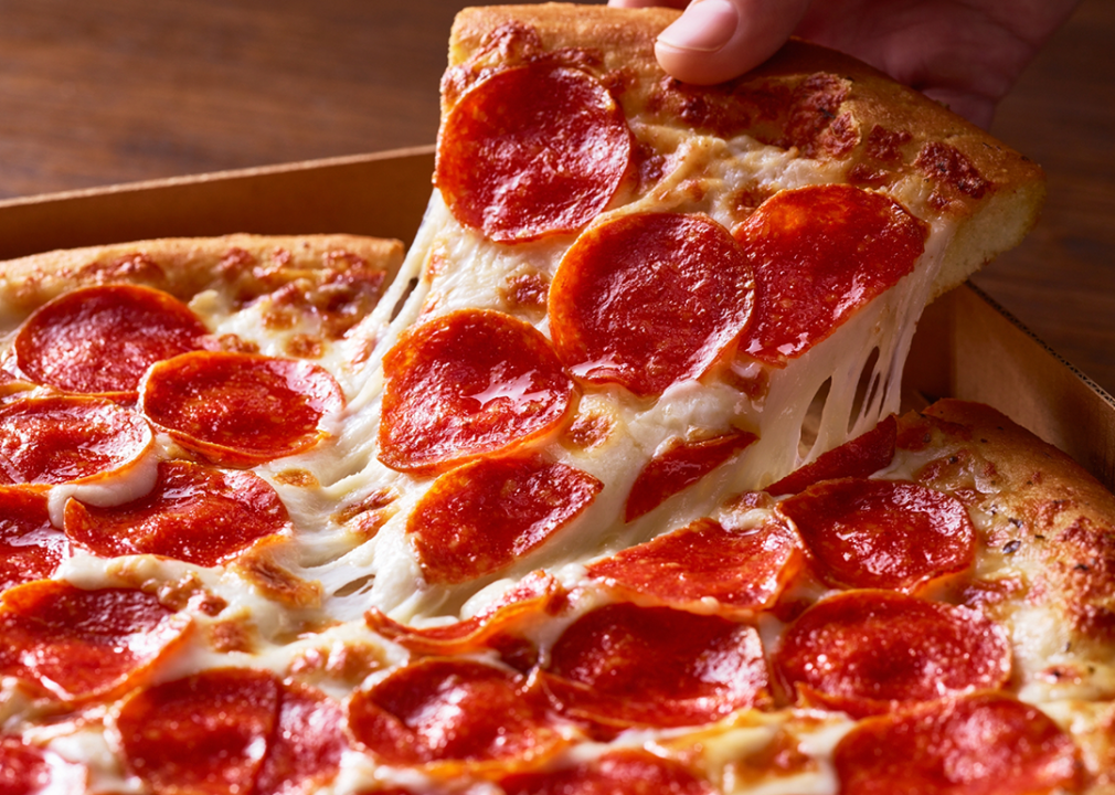 Hand taking pepperoni pizza slice out of a box.