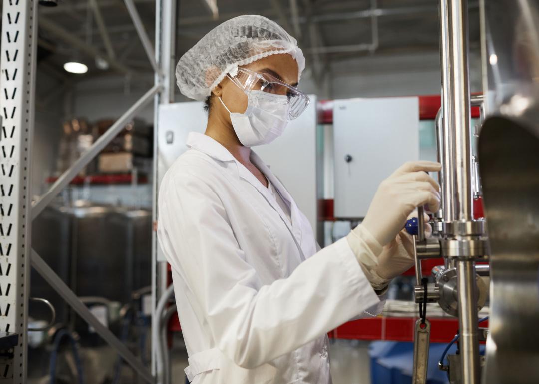 Woman wearing protective clothing operating equipment at chemical plant.