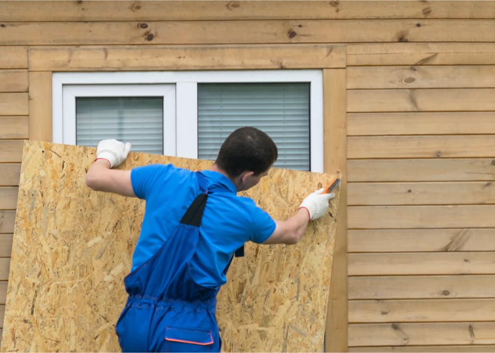 Photo shows a man putting plywood over a house window in preparation for a storm