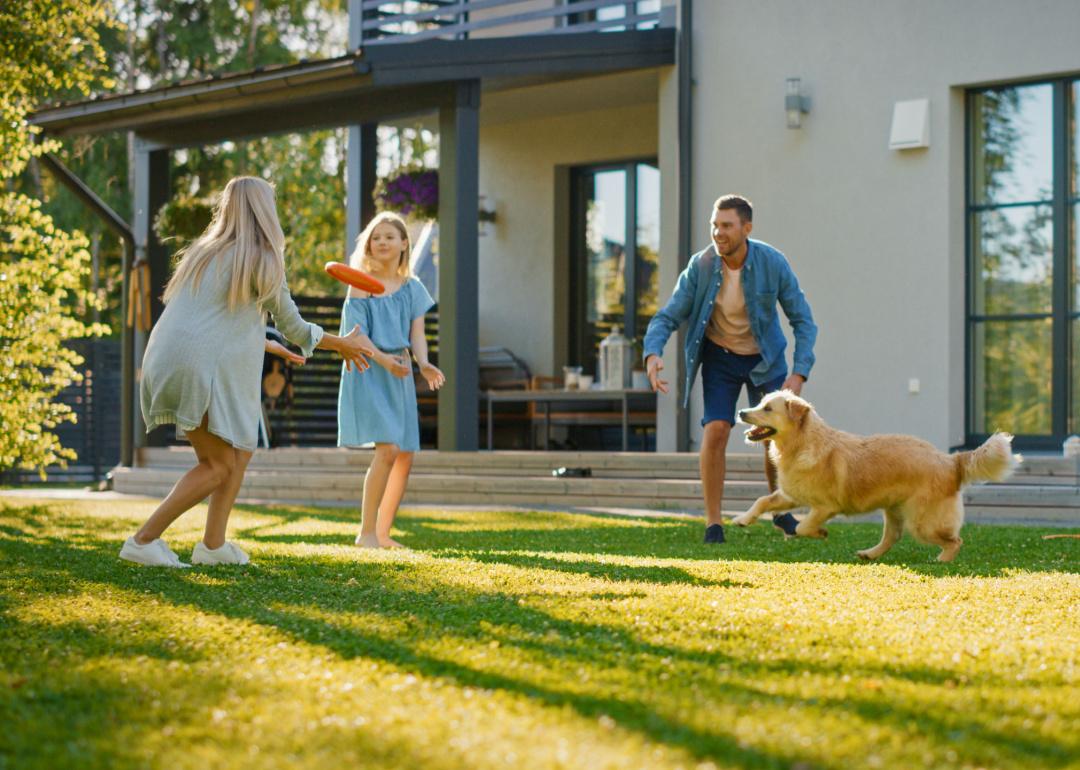 Family playing fetch with dog in backyard.