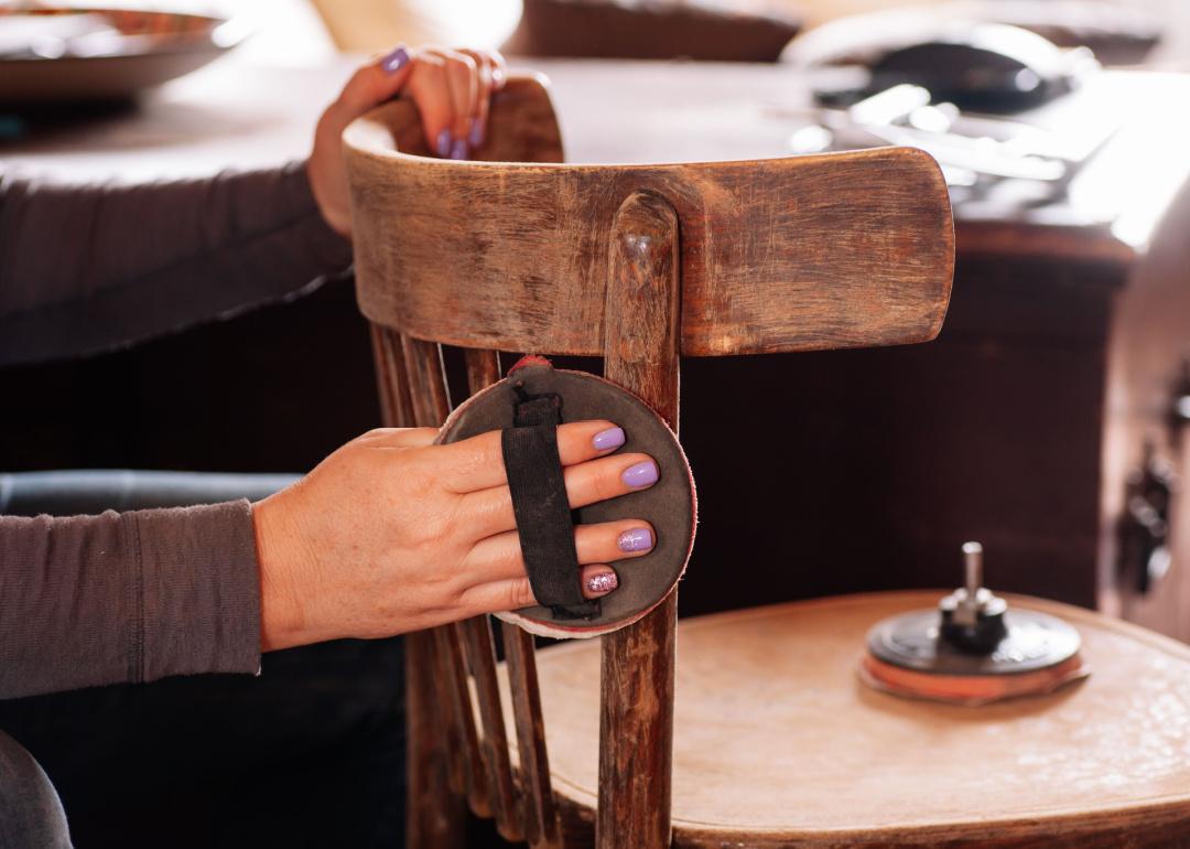 Person sanding surface of wooden chair.