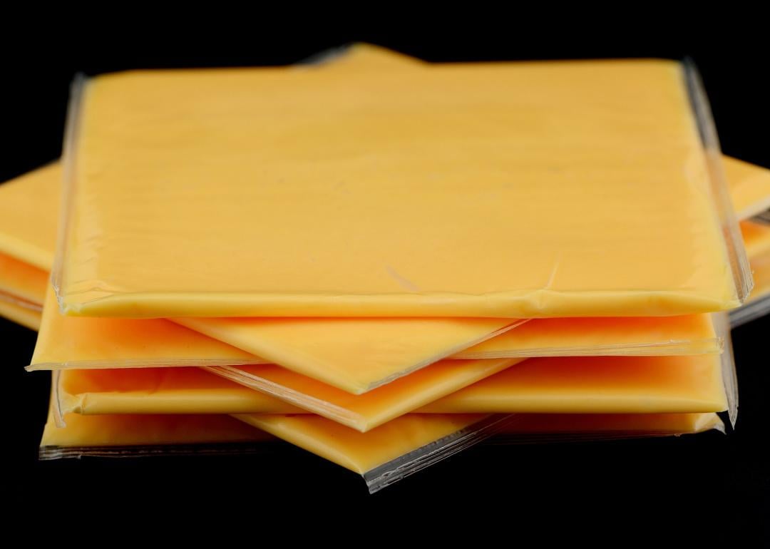 Slices of individually wrapped cheese on black background.