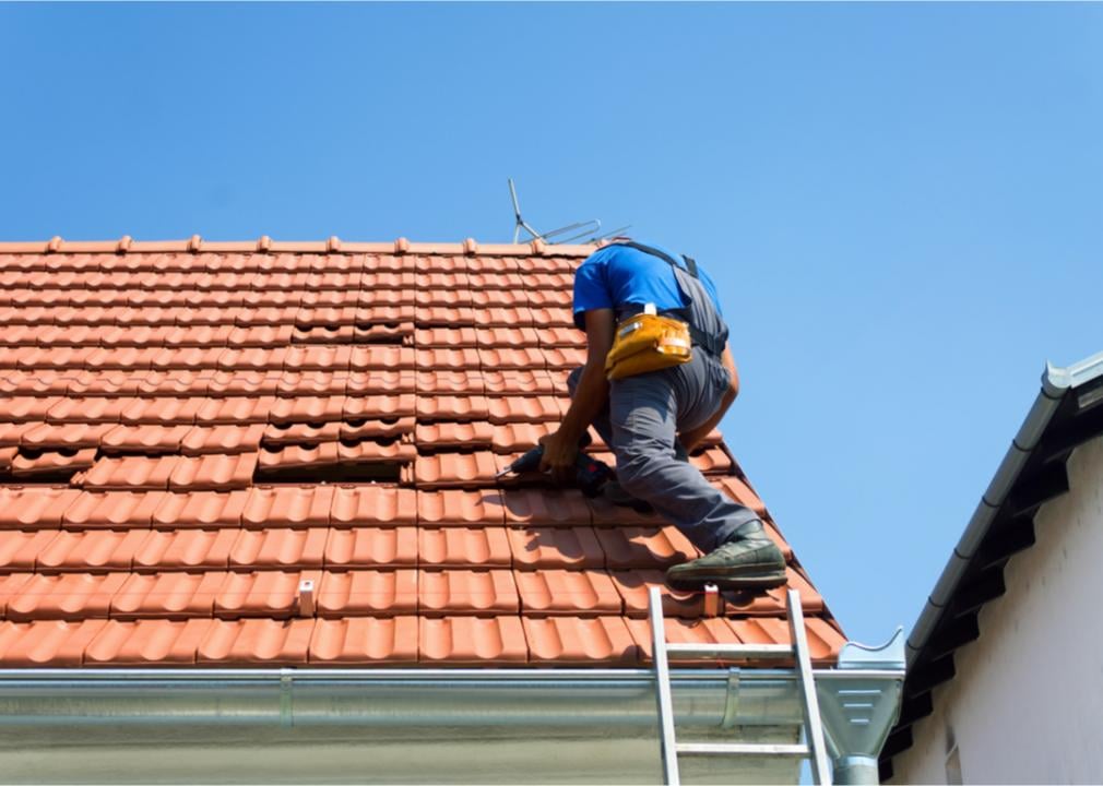 Photo shows a man on a ladder make repairs to a roof