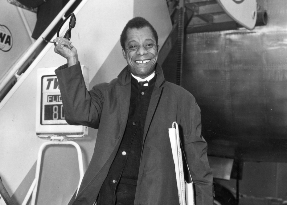 James Baldwin waves from tarmac by airplane.