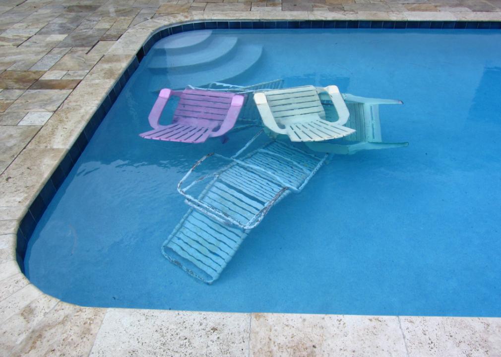 Photo shows four deck chairs submerged in a swimming pool