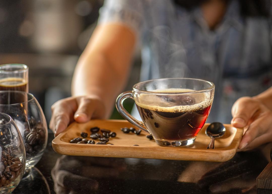 Barista serving glass cup of coffee on tray.