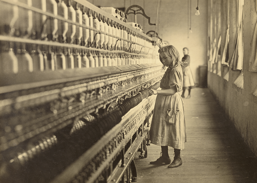 A young girl tends the spinning machine at a cotton mill.