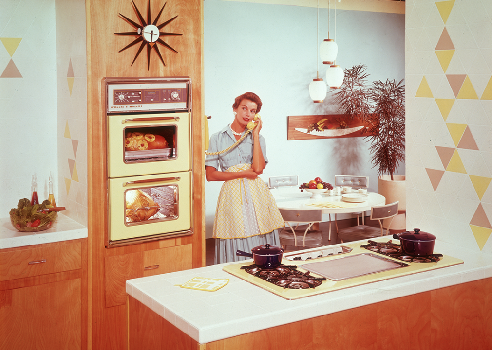 A woman stands talking on the phone in the kitchen.