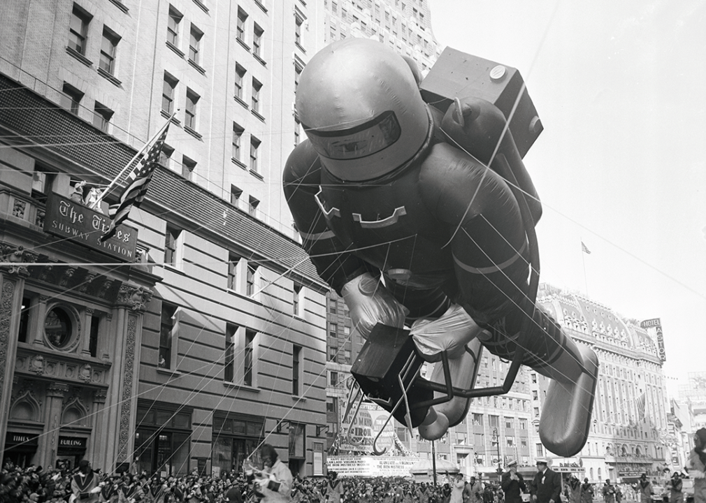 A giant spaceman balloon floats down street, passing The Times Subway Station.