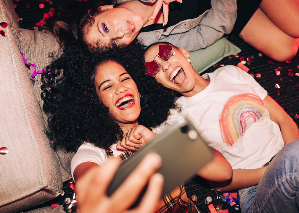 Three friends taking a selfie while lying on the floor at a party.