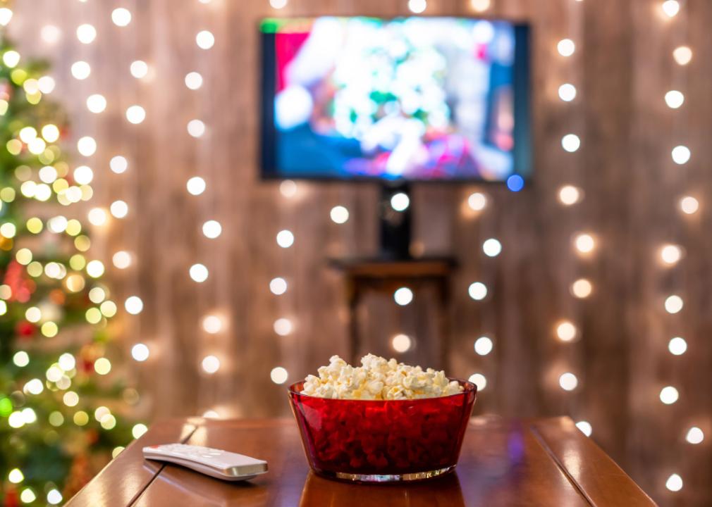 Christmas lights, a tree, TV, remote and popcorn in a living room.