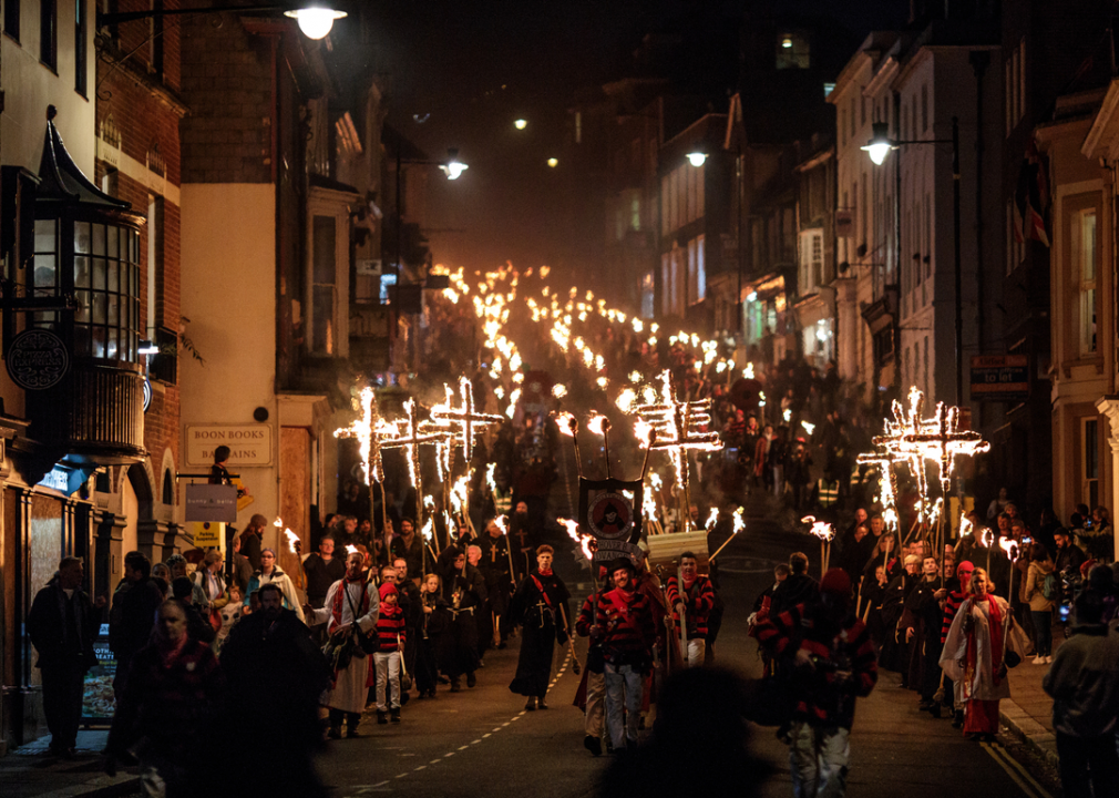 At night, people carrying lit crosses and sticks walk down a street.