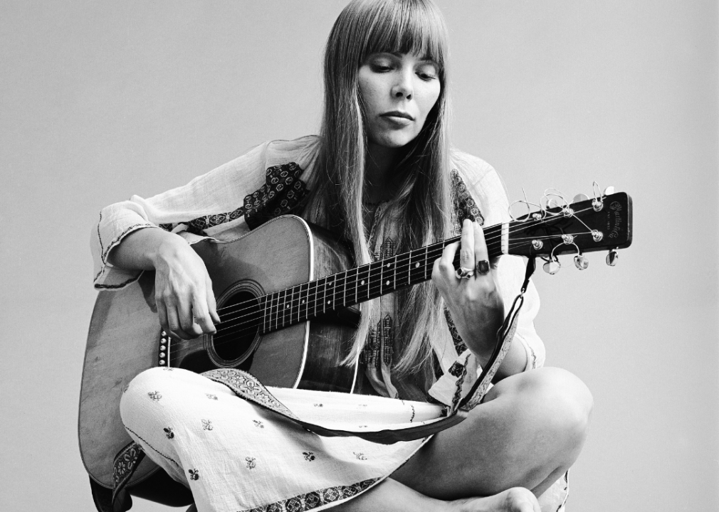 Joni Mitchell in sitting pose while playing guitar.