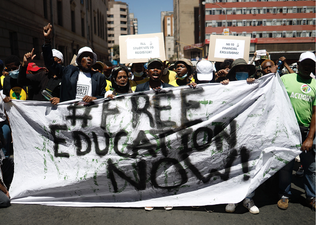 A group of people hold a large piece of a fabric that says, # free education now. Others hold signs that say, all students to register and no to financial exclusions.